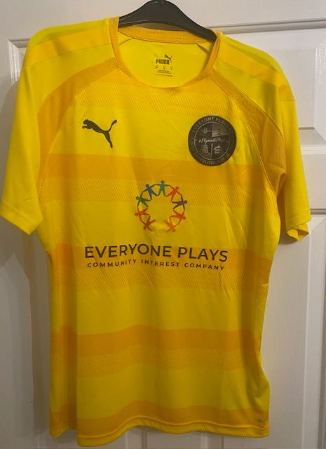 Plymouth Plays Community Team shirt, front, on a hanger